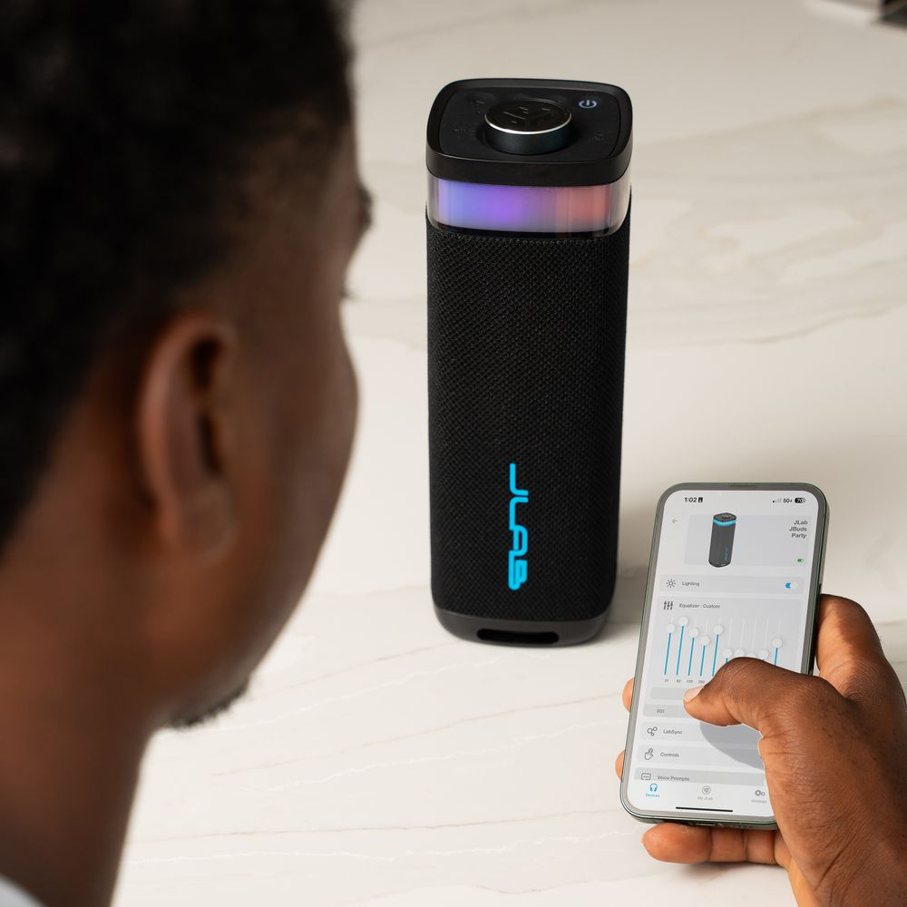Un uomo usa uno speaker con un'app sul telefono. Lo speaker ha luci colorate.