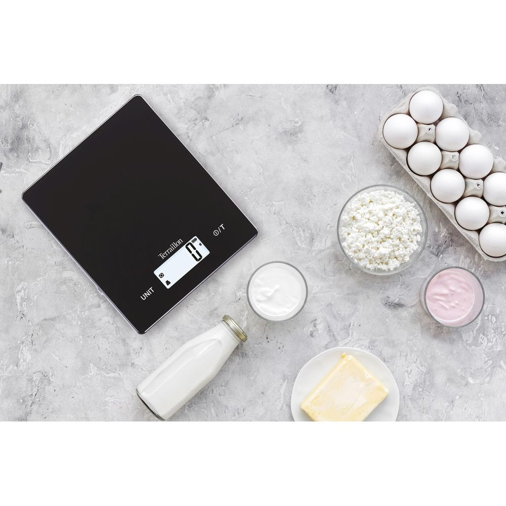 Une balance de cuisine numérique noire avec des œufs, du fromage blanc, du yaourt, du lait et du beurre.