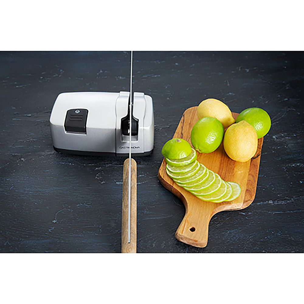 Srebrna ostrzałka do noży z nożem, obok drewniana deska z plasterkami limonki i cytryny.