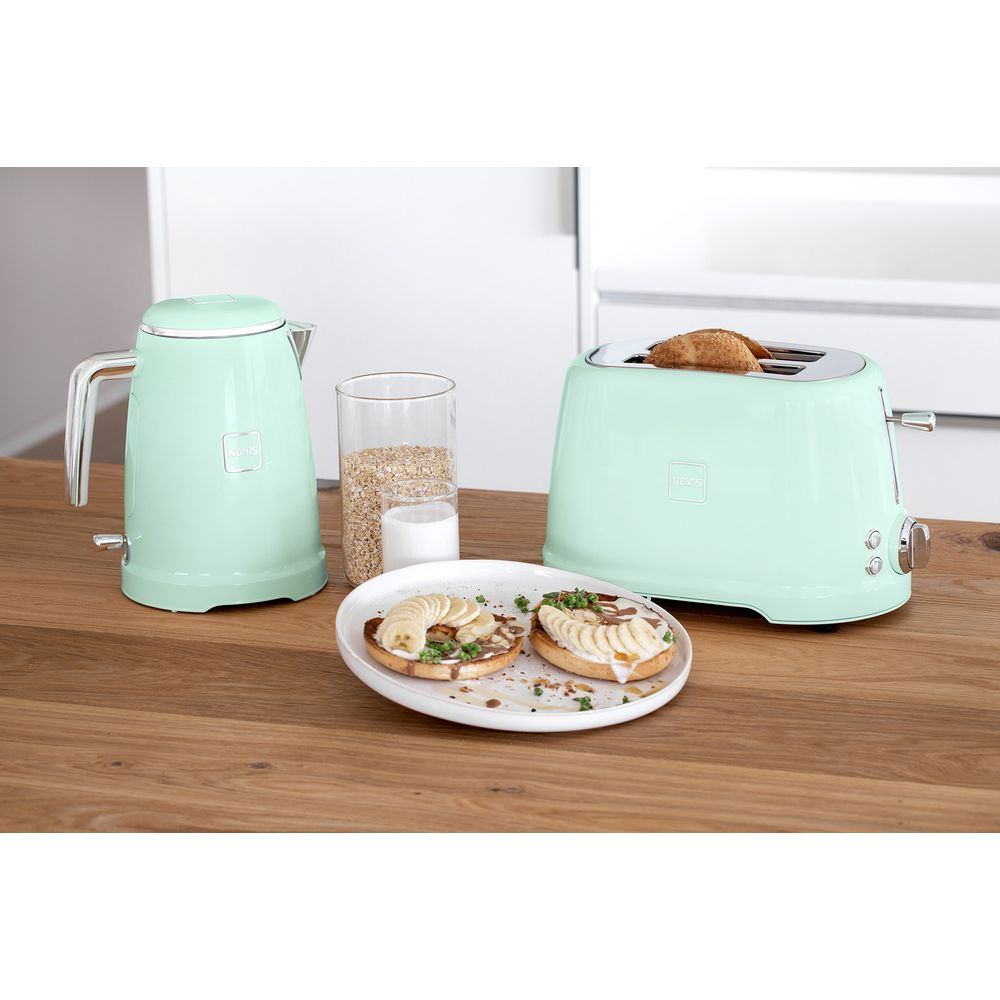 Ein mintgrüner Wasserkocher und Toaster auf einem Holztisch mit Toast und Obst.