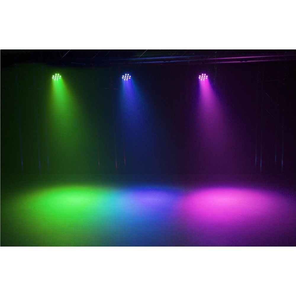 Tres luces de escenario proyectan haces verdes, azules y morados en una sala oscura y humeante.