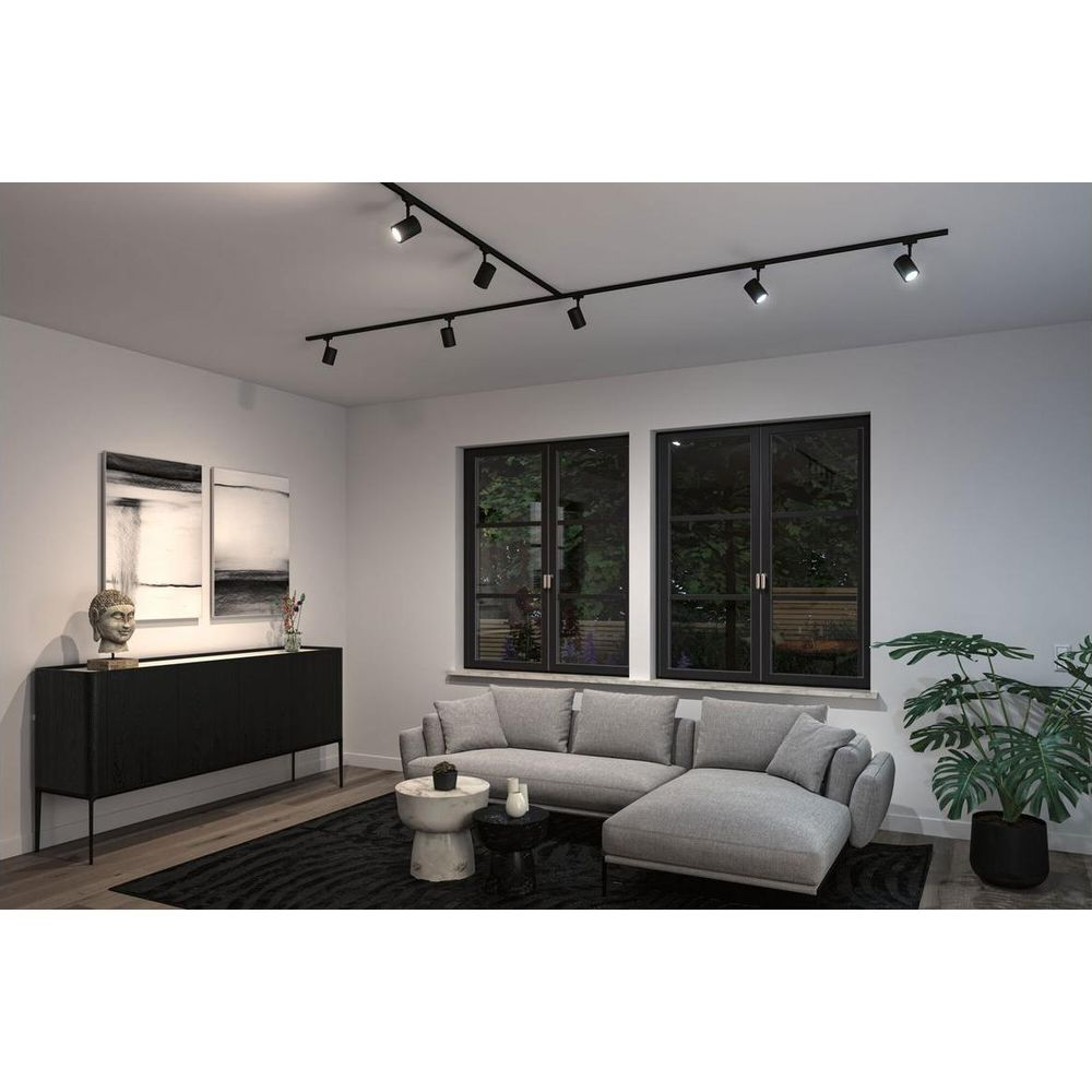 Nowoczesny salon z szarą sofą narożną, czarną komodą i oświetleniem szynowym.