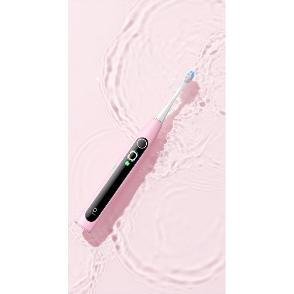 Eine rosafarbene elektrische Zahnbürste mit blau-weißen Borsten, die auf einer rosa Oberfläche mit Wasserspuren liegt.