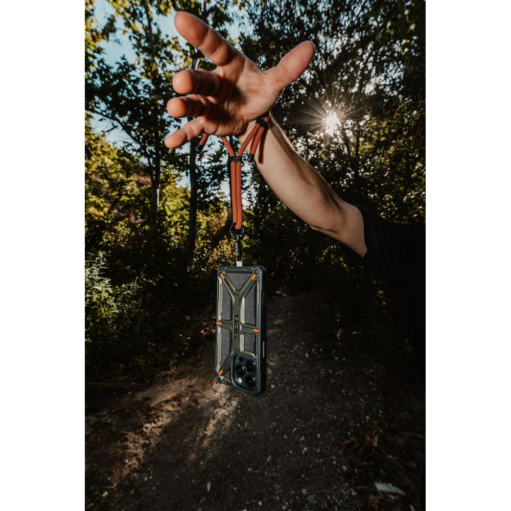 Hand hält Lanyard mit Handyhülle vor bewaldetem Hintergrund mit Sonnenlicht.