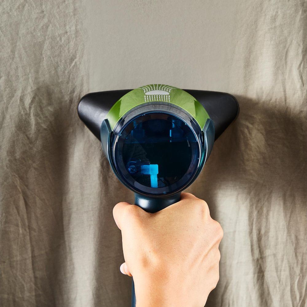 Una mano tiene una testina dell'aspirapolvere con serbatoio blu su tessuto beige.