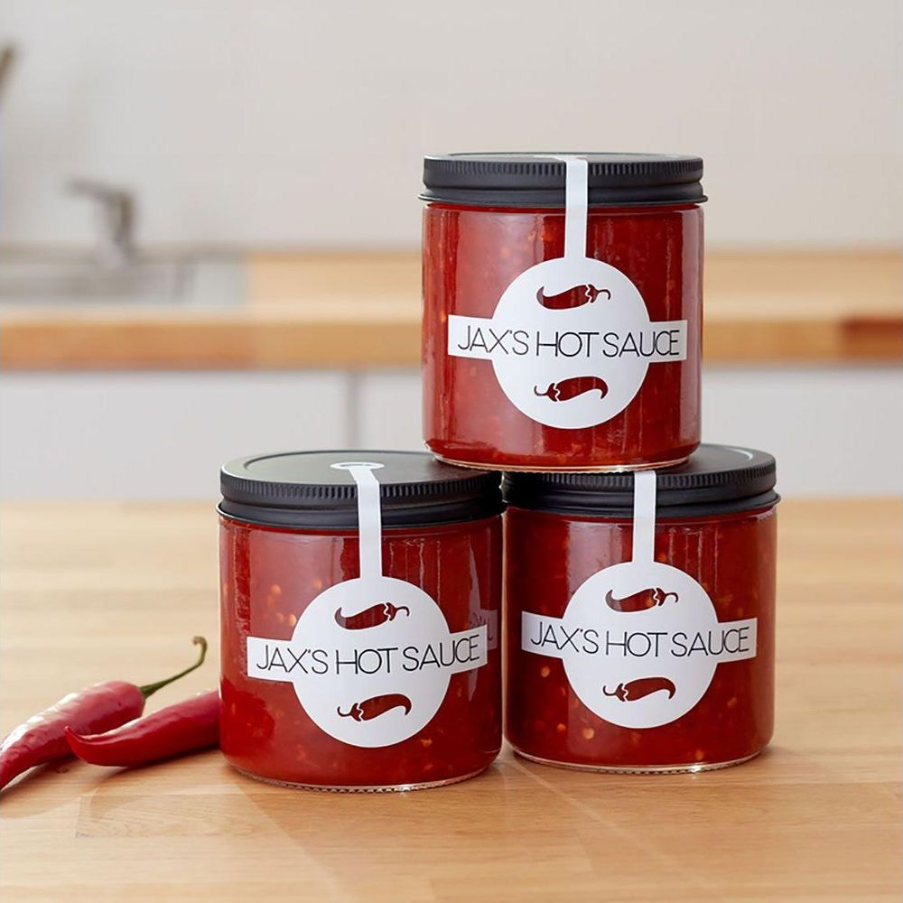 Drei Gläser Jax's Hot Sauce mit Chilis und Etiketten auf einem Holztisch.
