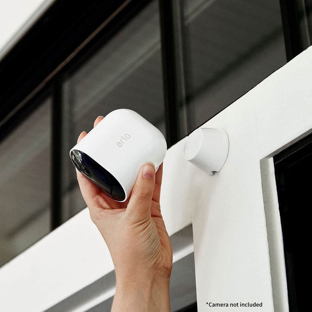 Eine Hand hält eine weiße Arlo-Kamera neben einer weißen Halterung.