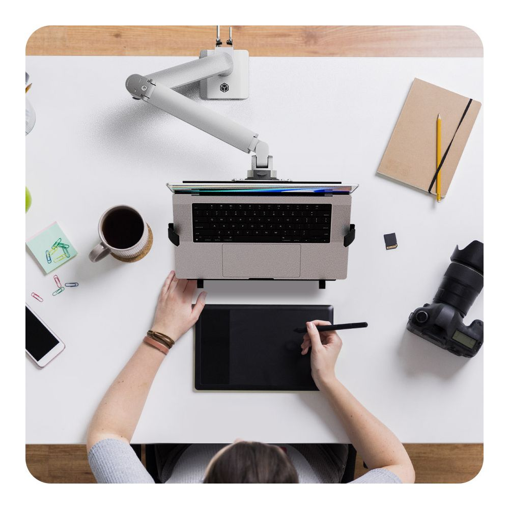 Vogelperspektive einer Person, die an einem Schreibtisch mit Kamera ein Grafiktablett und einen Laptop benutzt.