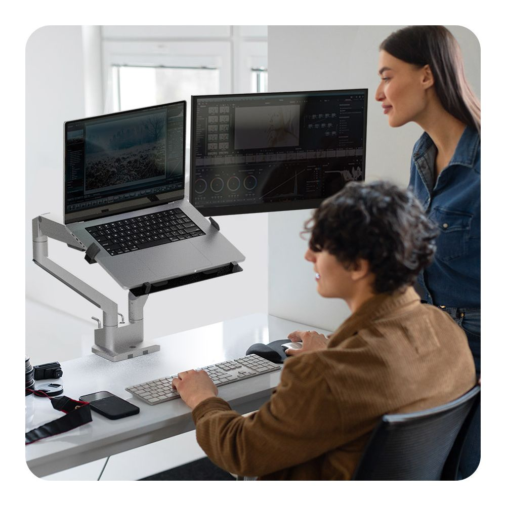 Zwei Personen arbeiten an einem Schreibtisch mit zwei Monitoren und einem Laptop.