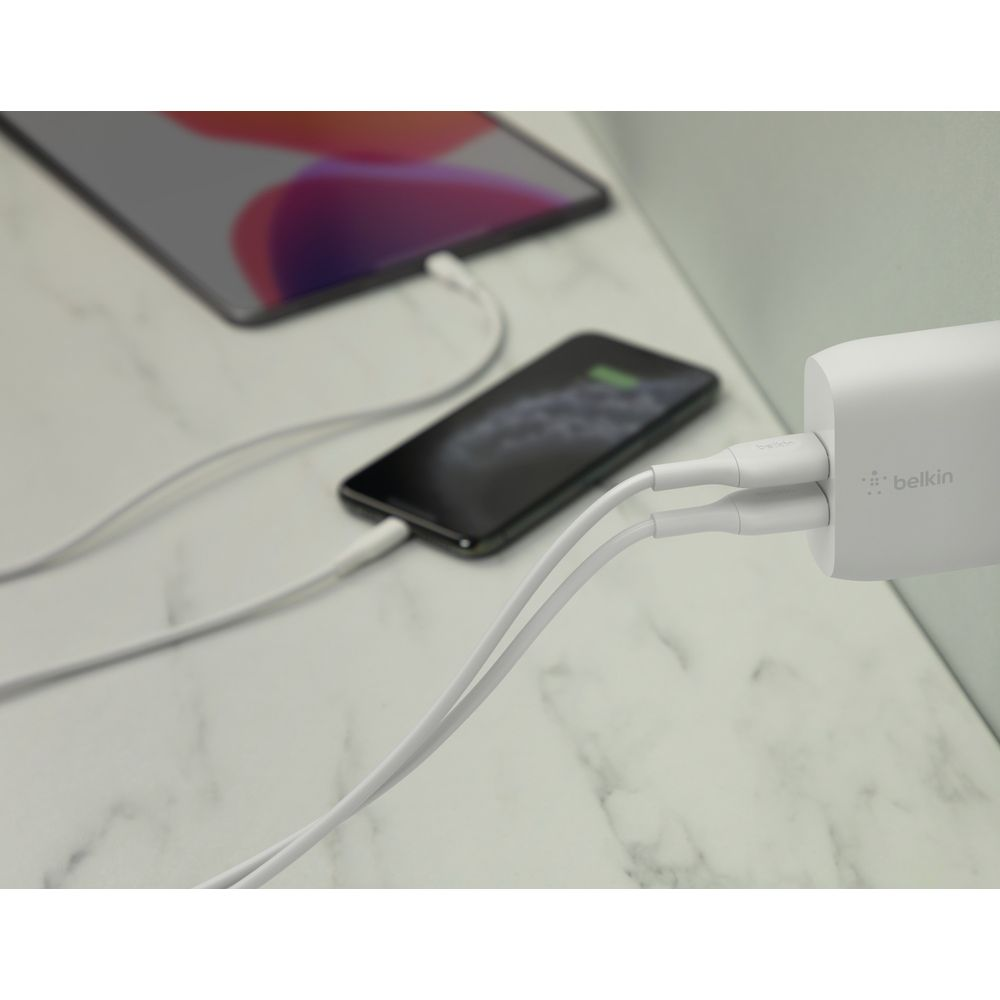 Un adattatore di ricarica Belkin bianco alimenta uno smartphone e un tablet tramite cavi bianchi.