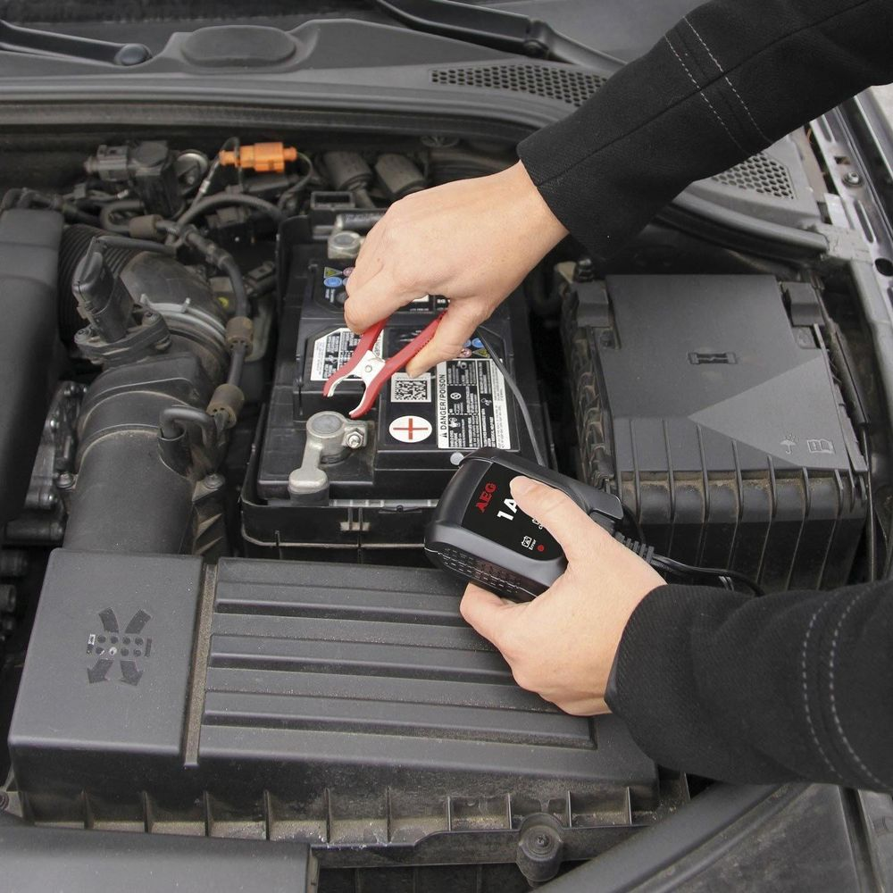 Eine Person klemmt ein Ladegerät an eine Autobatterie im Motorraum.
