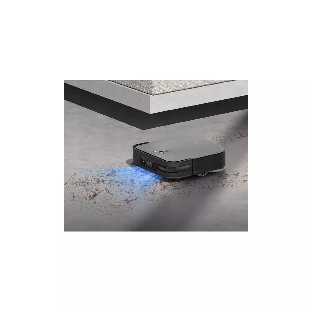 Ein grauer Saugroboter reinigt einen Betonboden neben einer Couch.