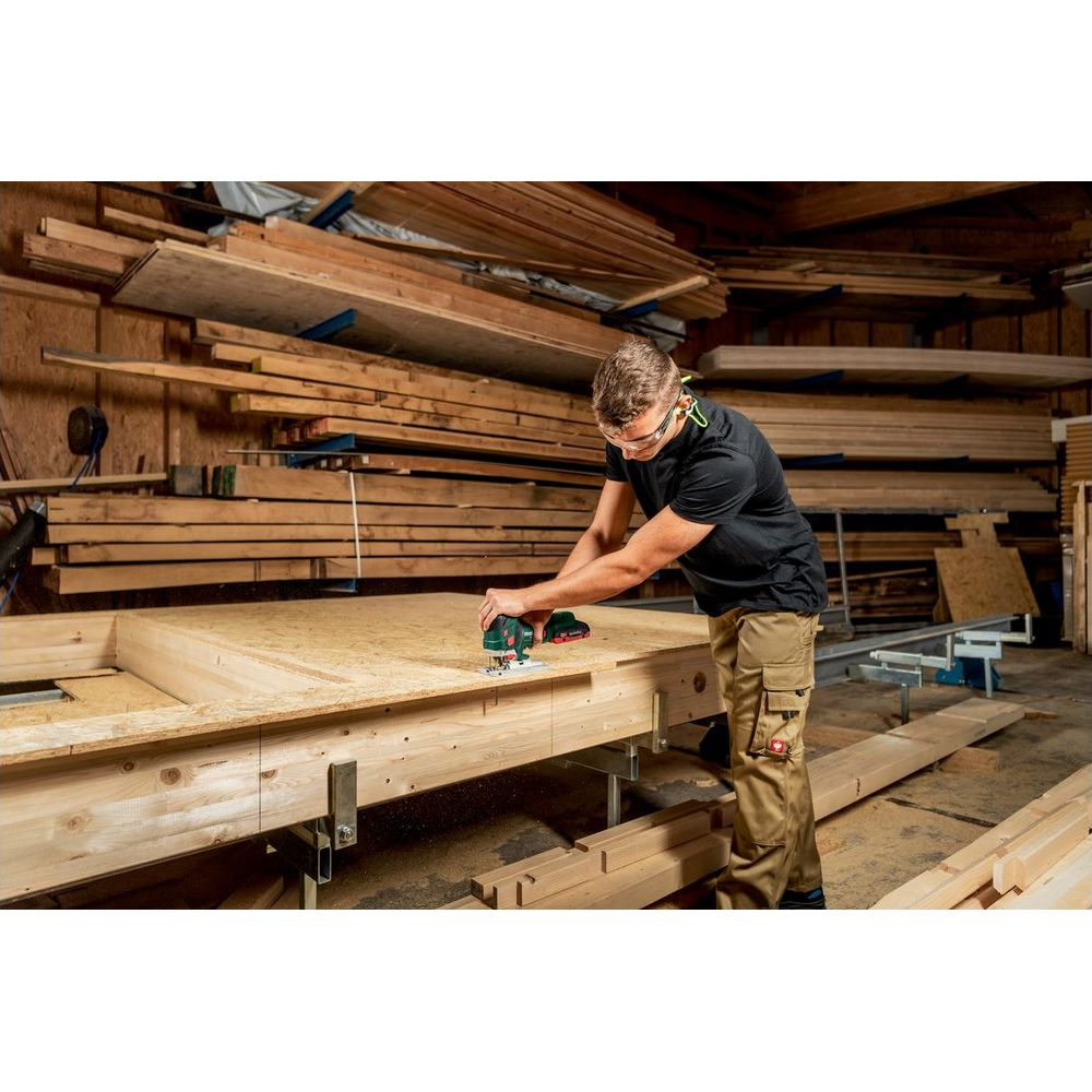 Mężczyzna używa wyrzynarki na stole warsztatowym, drewno w tle.