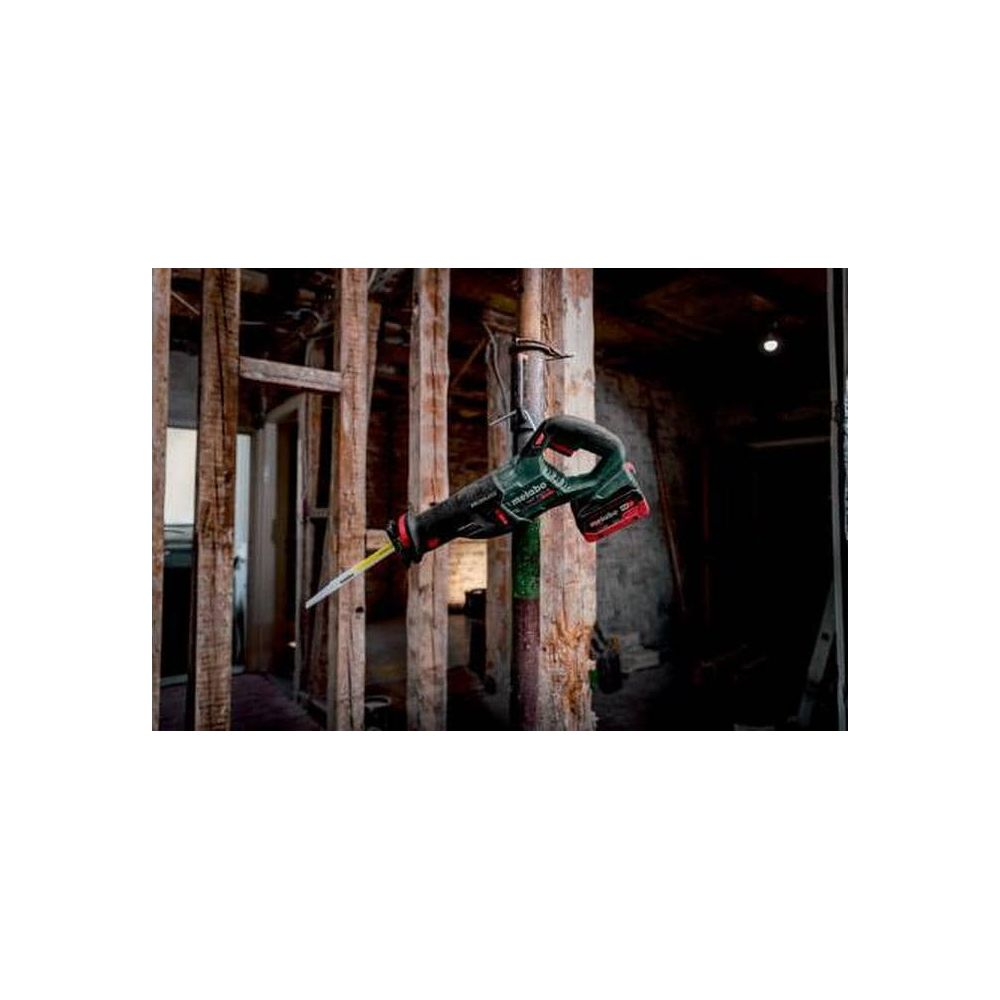 Szlifierka szablasta na akumulator wisi przed drewnianymi belkami w ciemnym pomieszczeniu.