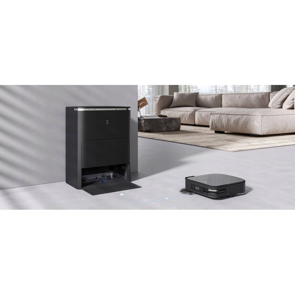 Czarny robot sprzątający porusza się po szarej podłodze w stronę czarnej stacji dokującej.