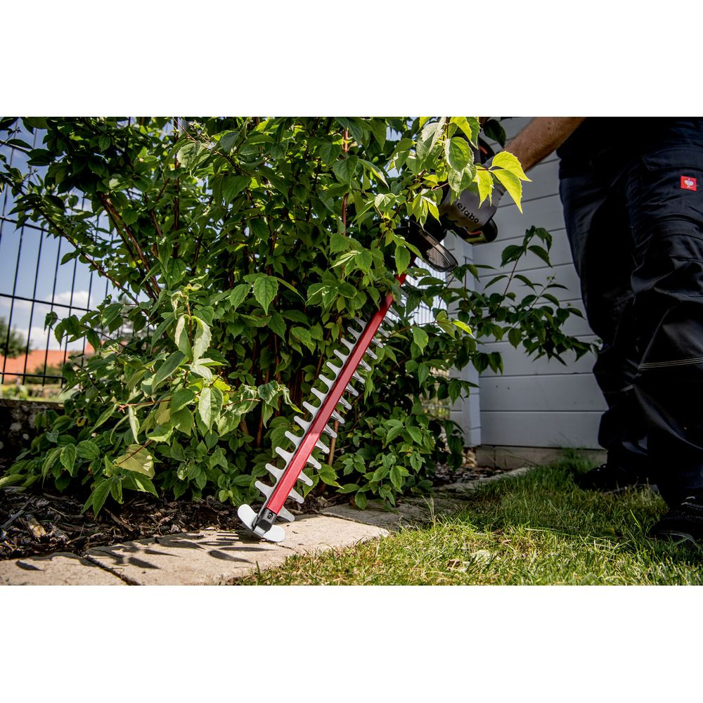 Osoba przycina krzak czerwonymi nożycami do żywopłotu.