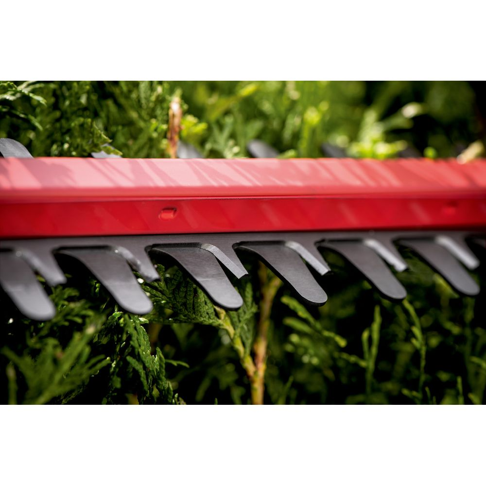 Zbliżenie czerwonych nożyc do żywopłotu z czarnymi ostrzami tnącymi zielone liście.