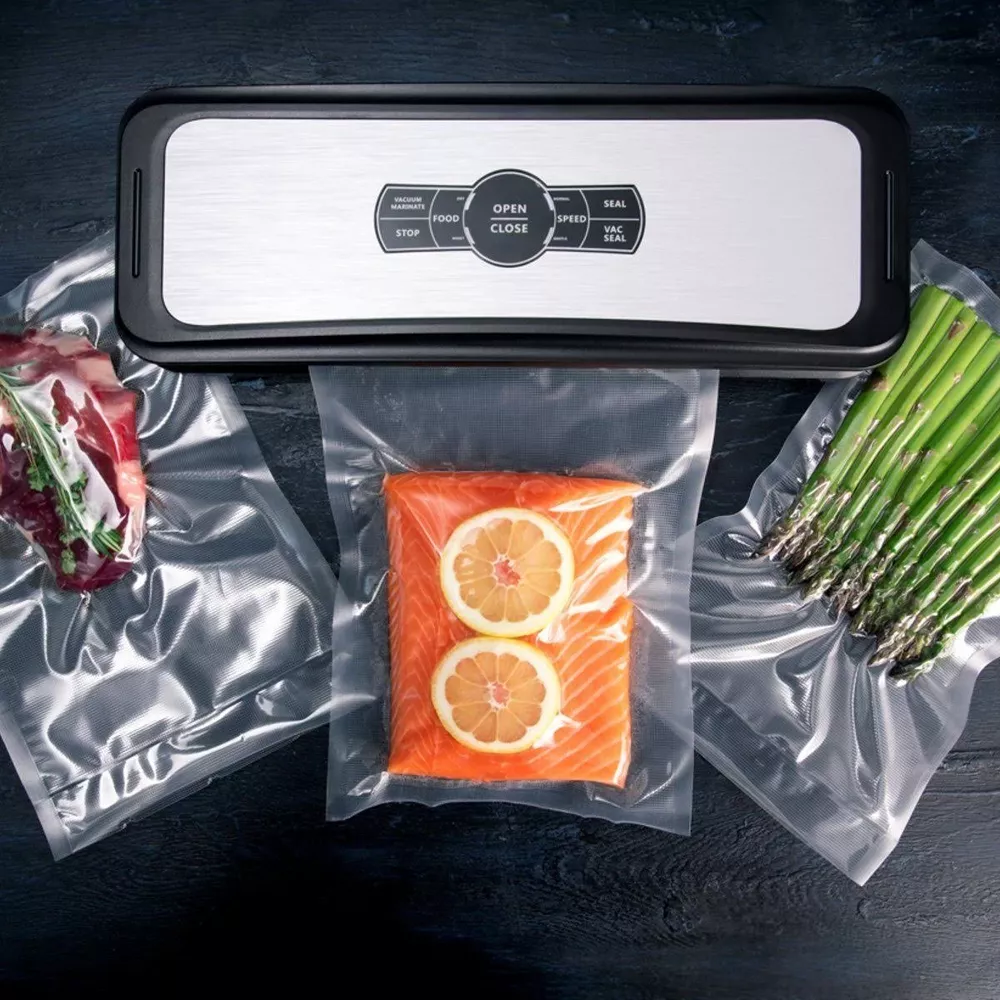 Ein Vakuumierer mit Fleisch, Lachs mit Zitrone und Spargel in Plastiktüten.