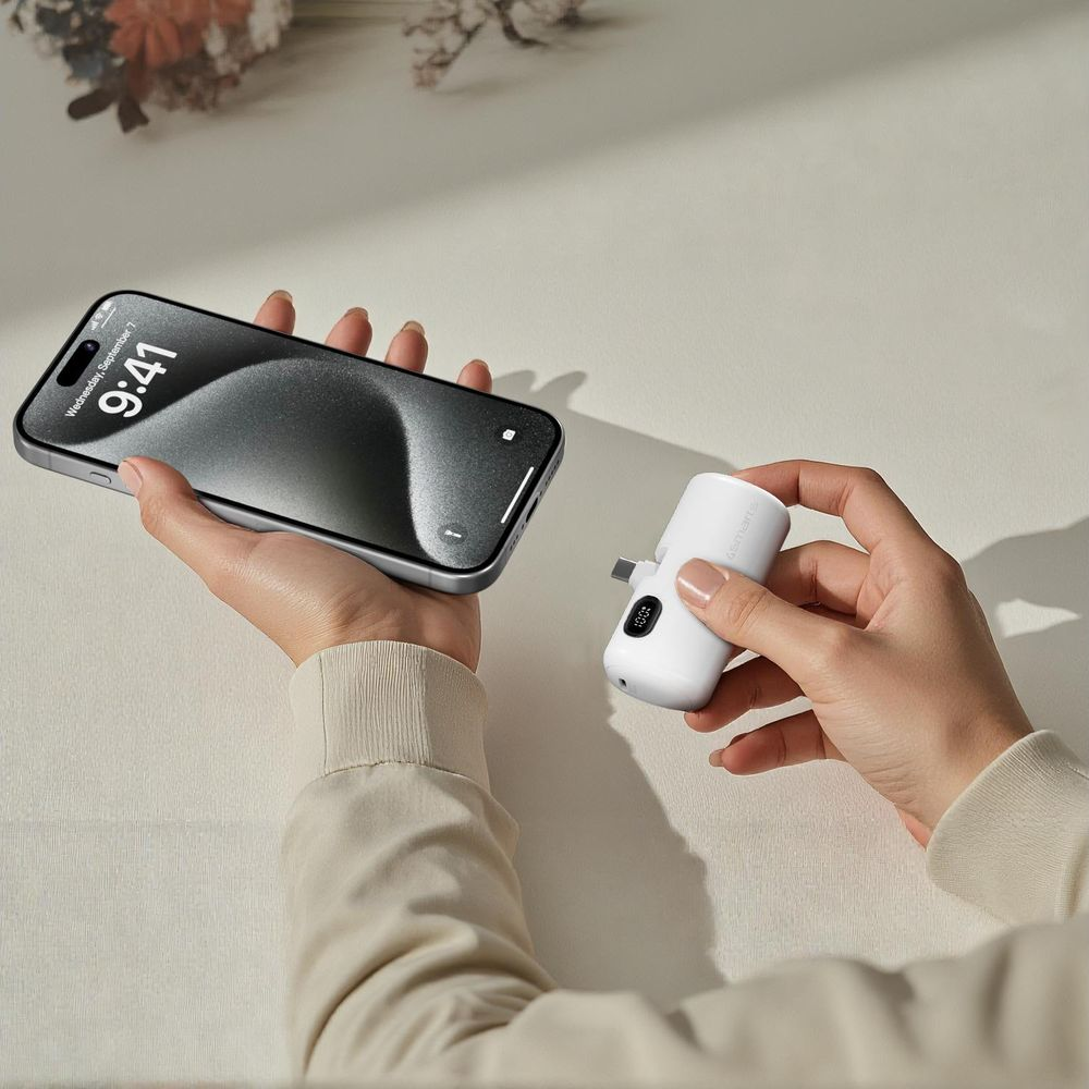 Una persona tiene in mano uno smartphone e un caricabatterie bianco.