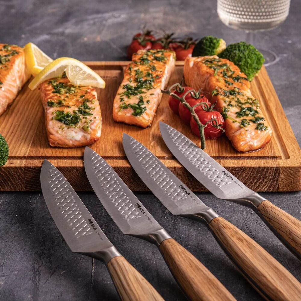 Cooked salmon with herbs, lemon, tomatoes, and broccoli on a wooden board with knives.