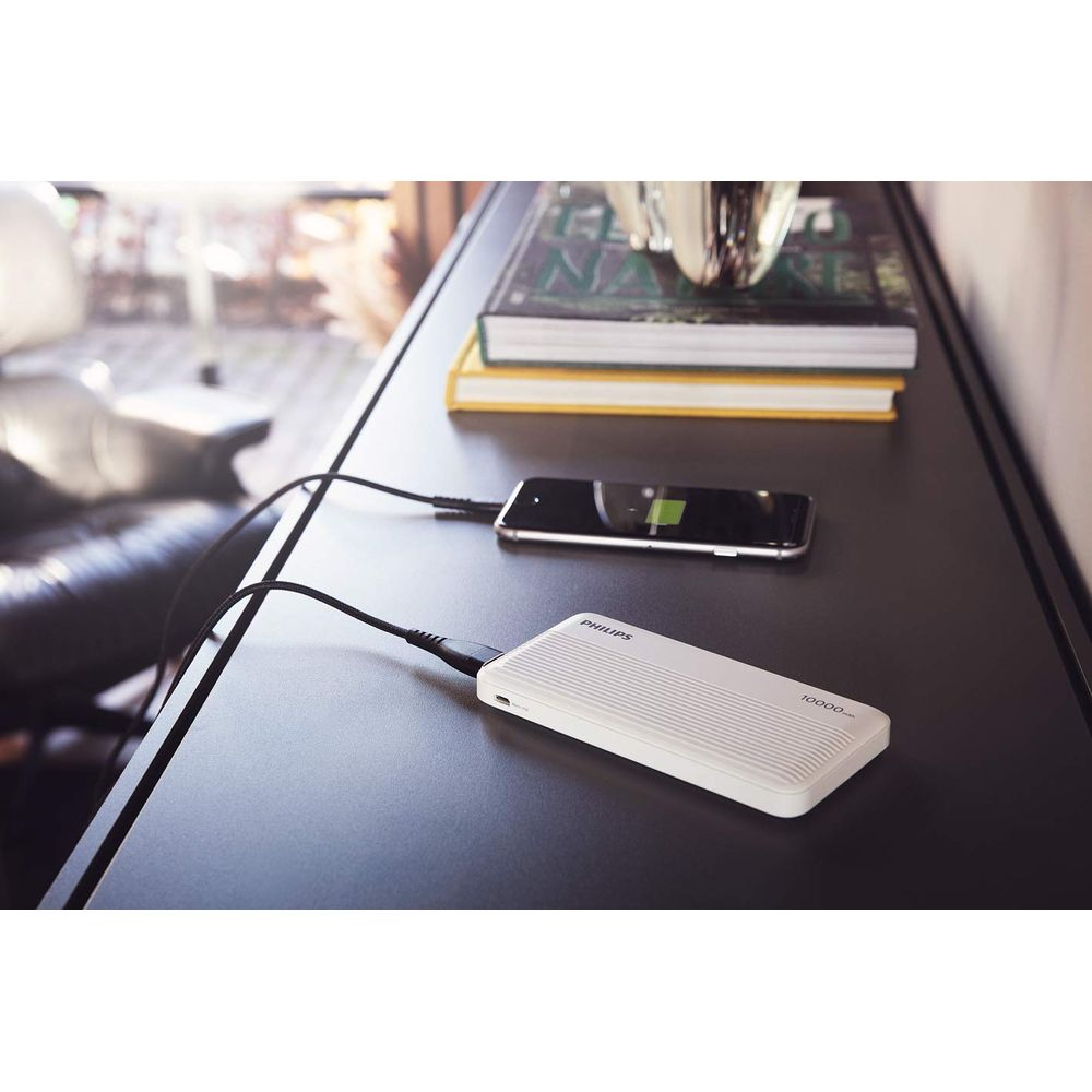 Une batterie externe Philips blanche charge un smartphone sur une table sombre.