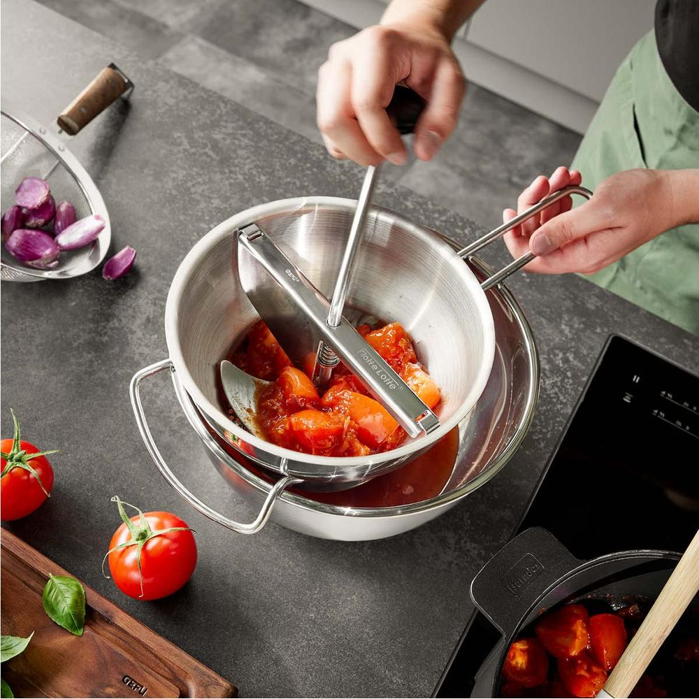 Person verarbeitet Tomaten in einem Passiergerät über einer Schüssel.