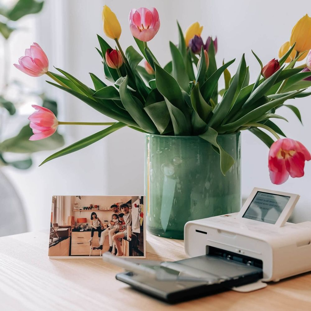 Un jarrón de tulipanes está sobre una mesa junto a una impresora fotográfica y una foto familiar enmarcada.