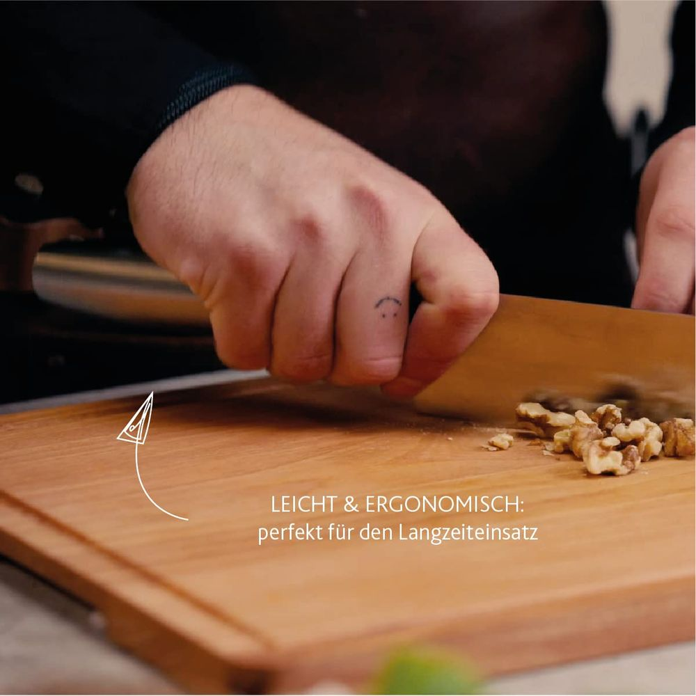 A hand chops walnuts on a wooden board. A smiley tattoo is visible.