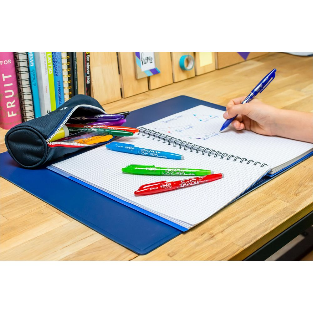 Kind schreibt in Notizbuch, Stifte liegen daneben, Bücher im Etui.