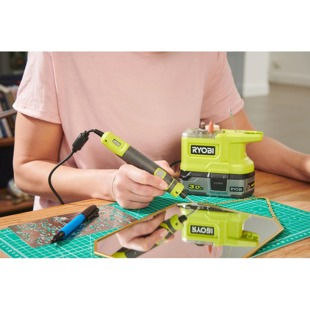 Persona incide specchio con attrezzo Ryobi. Tavolo in legno chiaro. Tappetino da taglio verde.