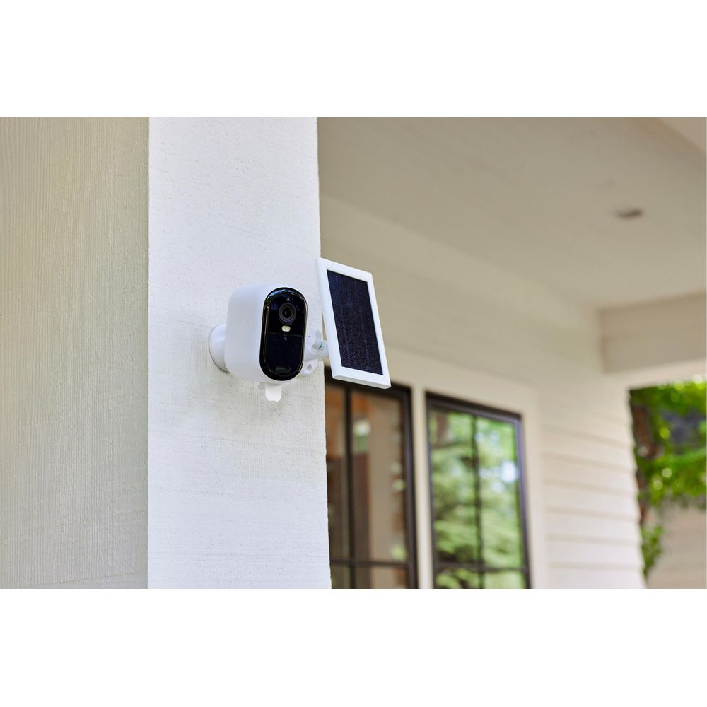 Biała kamera bezpieczeństwa z panelem słonecznym zamontowana na ścianie domu.