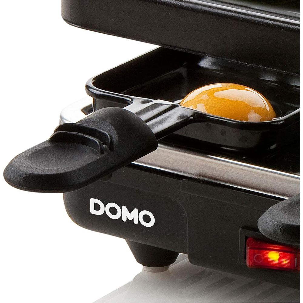 Ein rohes Ei in einer schwarzen Pfanne auf einem Domo-Grill mit rotem Licht.