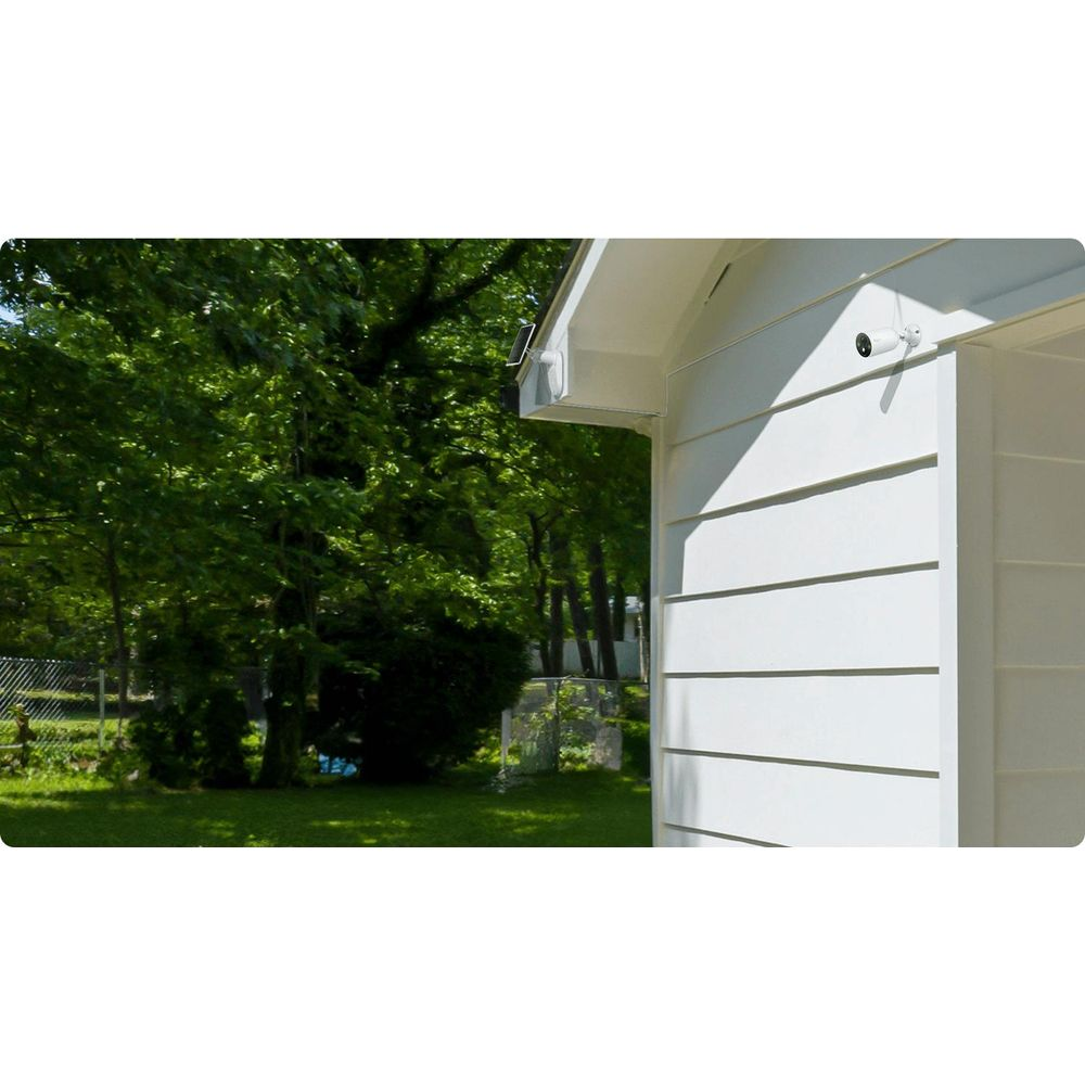 Biała kamera bezpieczeństwa zamontowana na białej ścianie domu pod okapem.