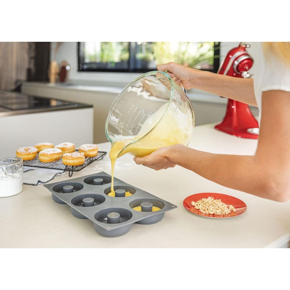 Flüssiger Teig wird aus einer Glasschüssel in eine Donutform gegossen.