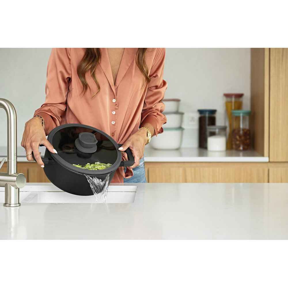 Een vrouw laat water uit een pot met groenten in een gootsteen lopen.