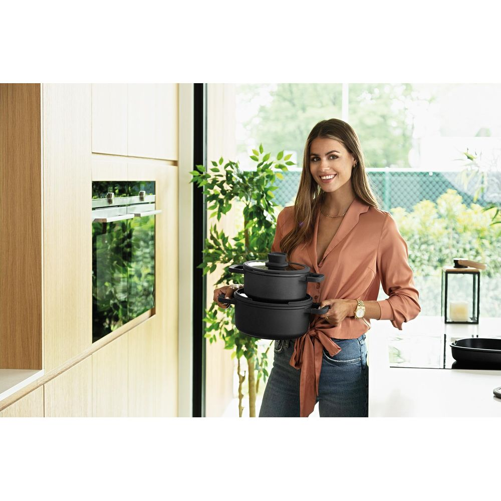 Een vrouw in een roze blouse houdt twee zwarte potten vast in een moderne keuken.