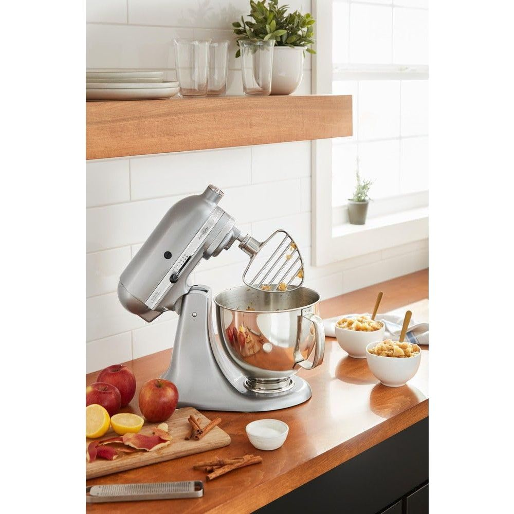 Silberner Standmixer mit Schüssel, Äpfel, Zitrone und Zimt auf einer Holzarbeitsplatte.