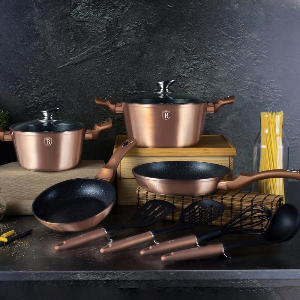 Batería de cocina y utensilios de color cobre con mangos negros sobre superficie oscura.