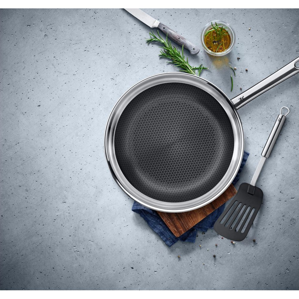 Stalowa patelnia z wzorem plastra miodu, łopatka i zioła.