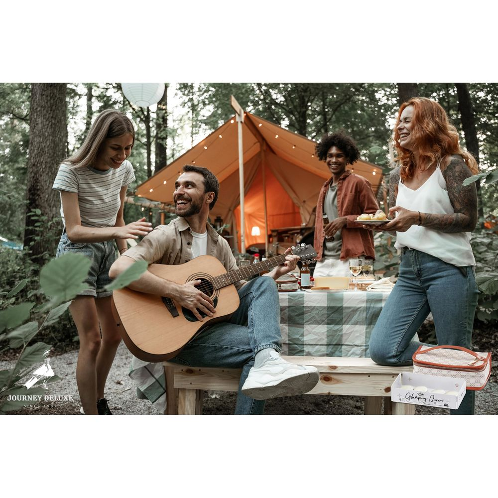 Freunde campen, Mann spielt Gitarre, Zelt im Hintergrund, Tisch mit Essen.