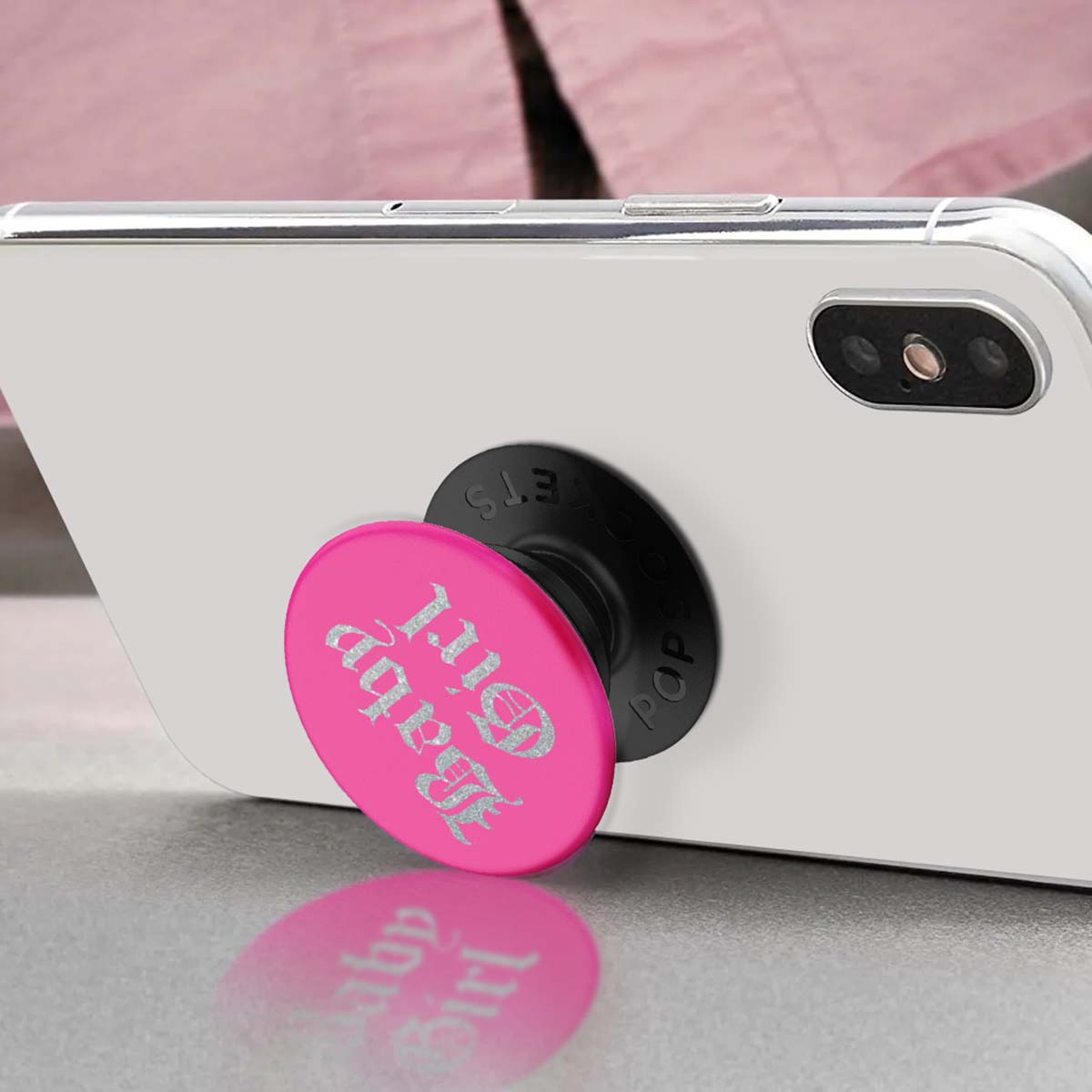 Un PopSocket rosa con testo "Baby Girl" su uno smartphone bianco.