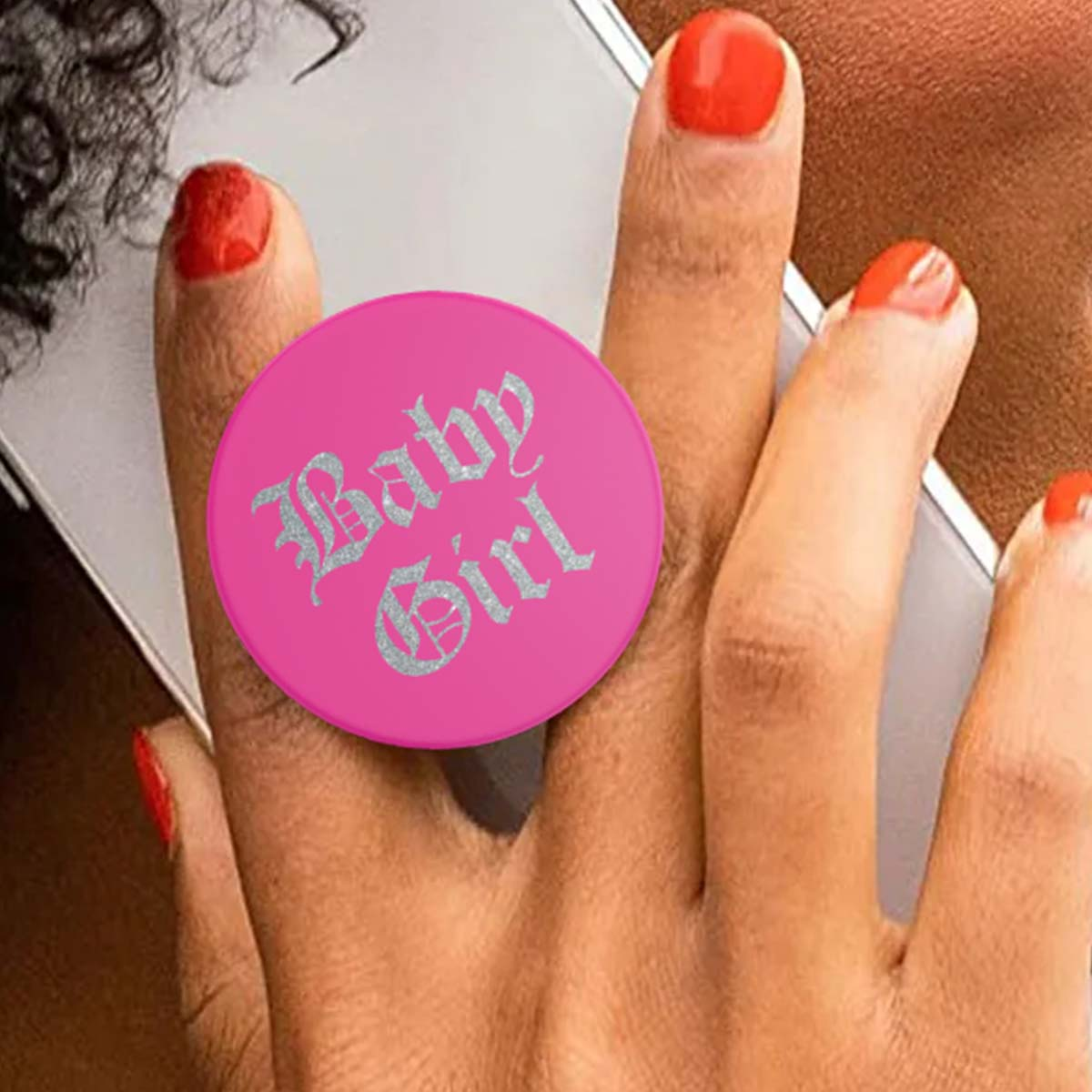 Una mano con unghie rosse tiene un telefono con un'impugnatura rosa "Baby Girl".