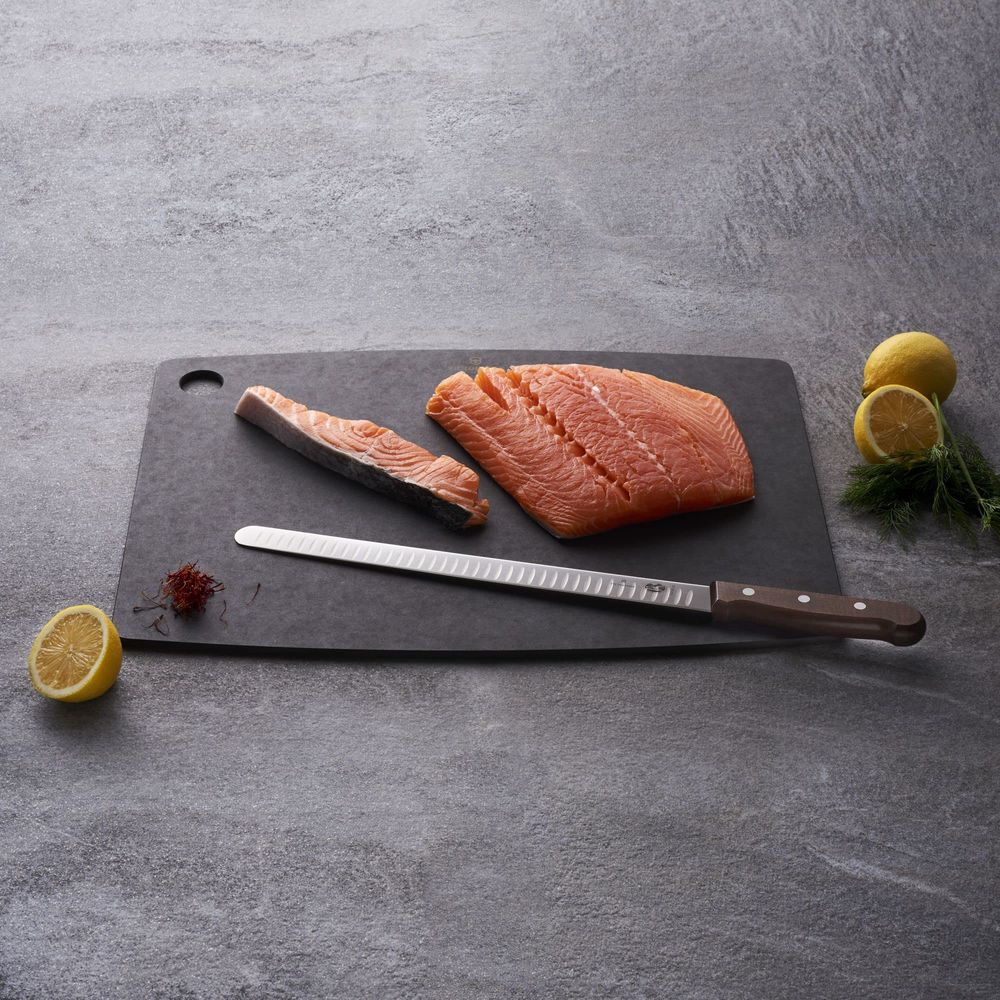 Rohes Lachsfilet und ein Stück auf einem schwarzen Brett mit Zitrone, Dill und einem Messer.