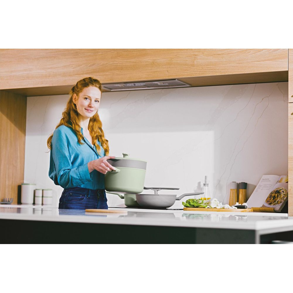 Een roodharige vrouw houdt een groene pan vast in een moderne keuken.