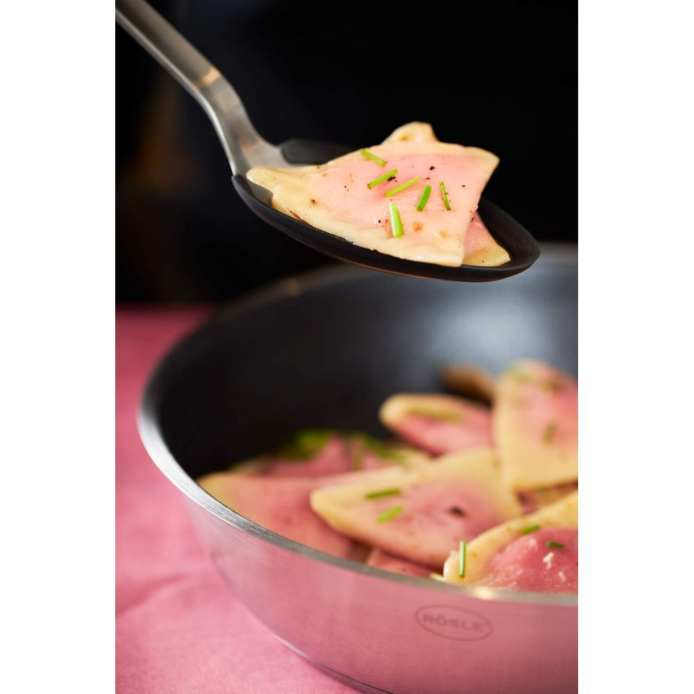 Ein Kochlöffel hebt eine Ravioli mit rosa Füllung und Schnittlauch aus einer Pfanne.