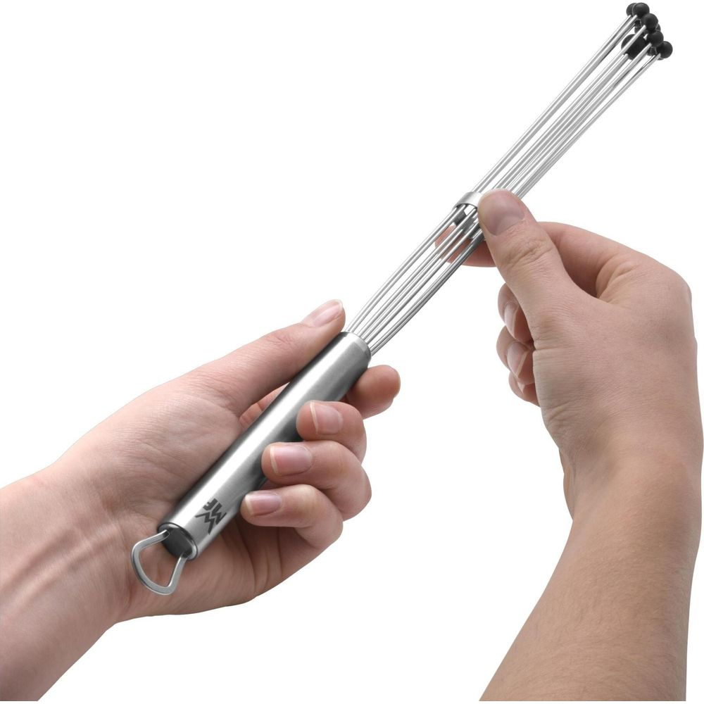 Dłonie trzymające smukłą, metalową trzepaczkę z czarnymi końcówkami.