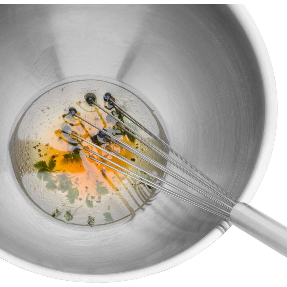 Trzepaczka miesza jajka i zioła w misce ze stali nierdzewnej.