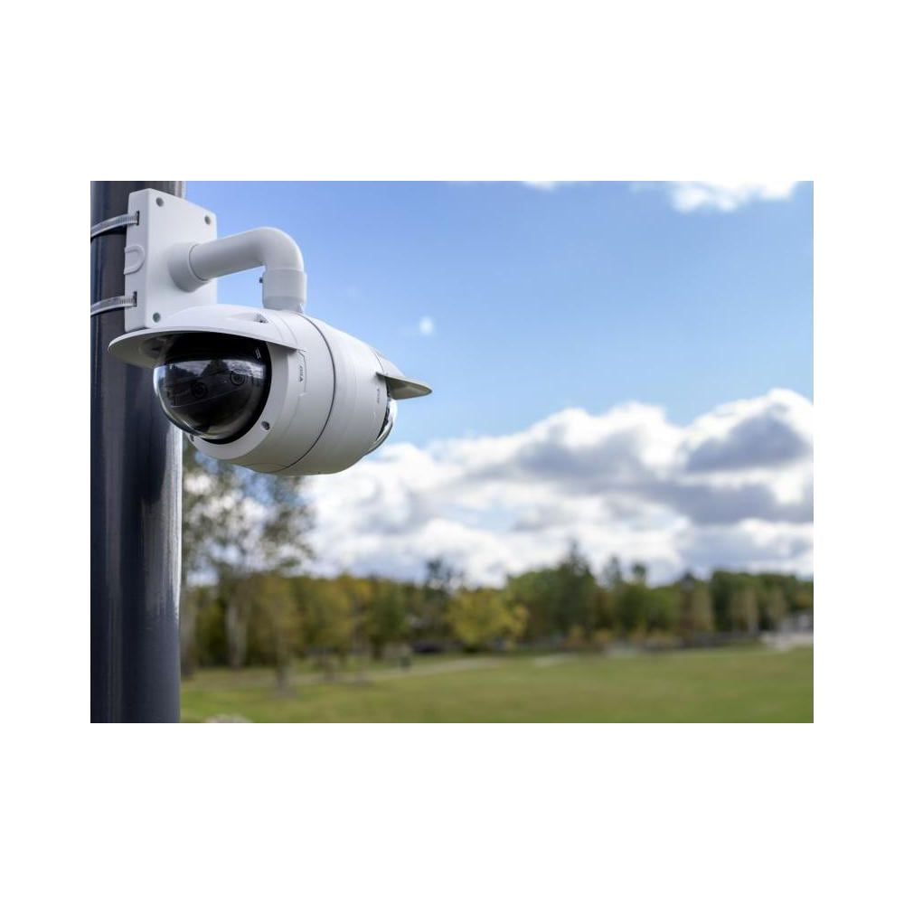 Biała kamera bezpieczeństwa zamontowana na słupie, z drzewami i niebem w tle.