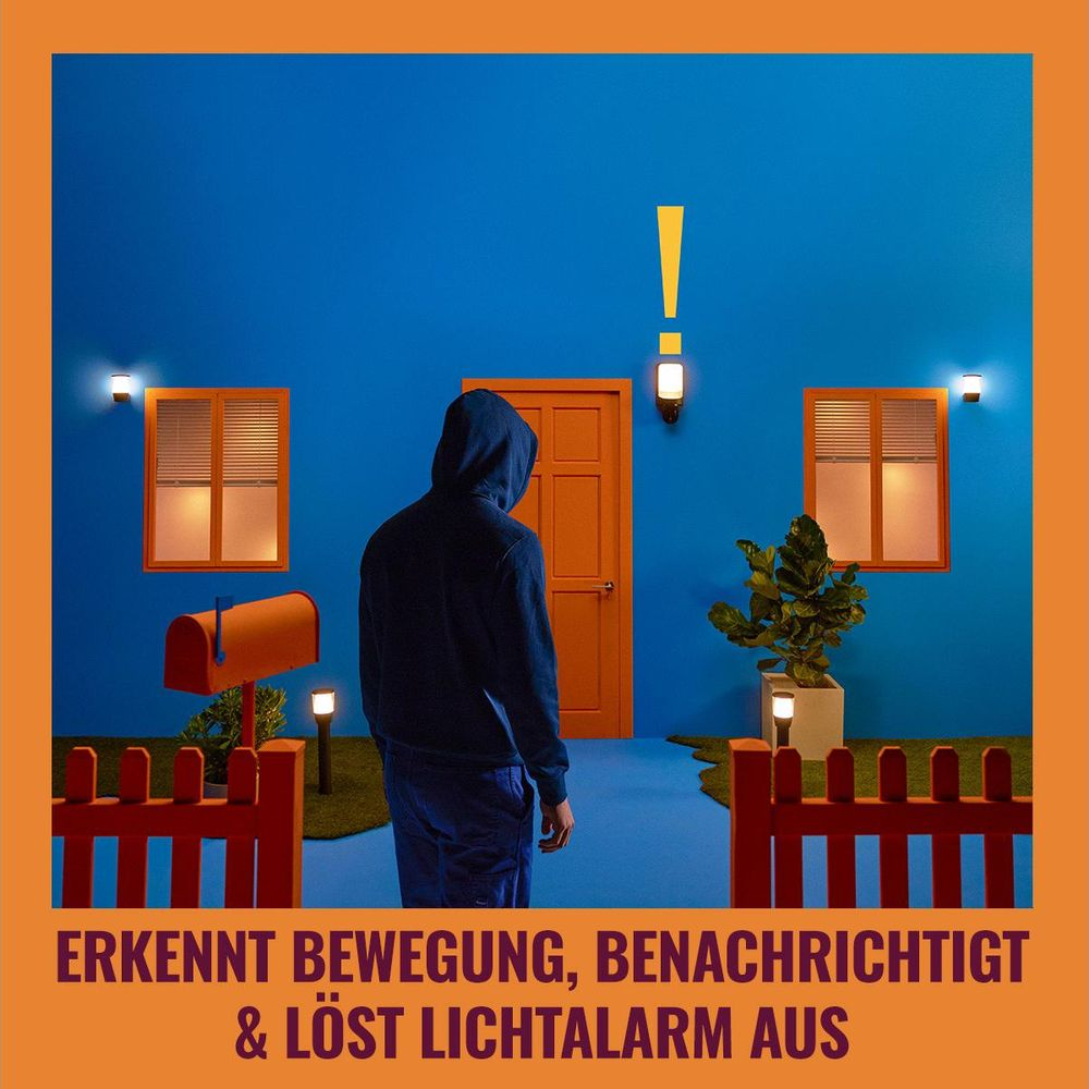 Man in hoodie facing blue house with orange windows and door. Detects motion.