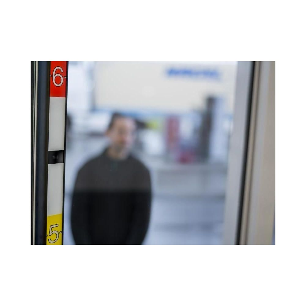 Mężczyzna w swetrze stoi za szybą z widocznymi cyframi 5 i 6.